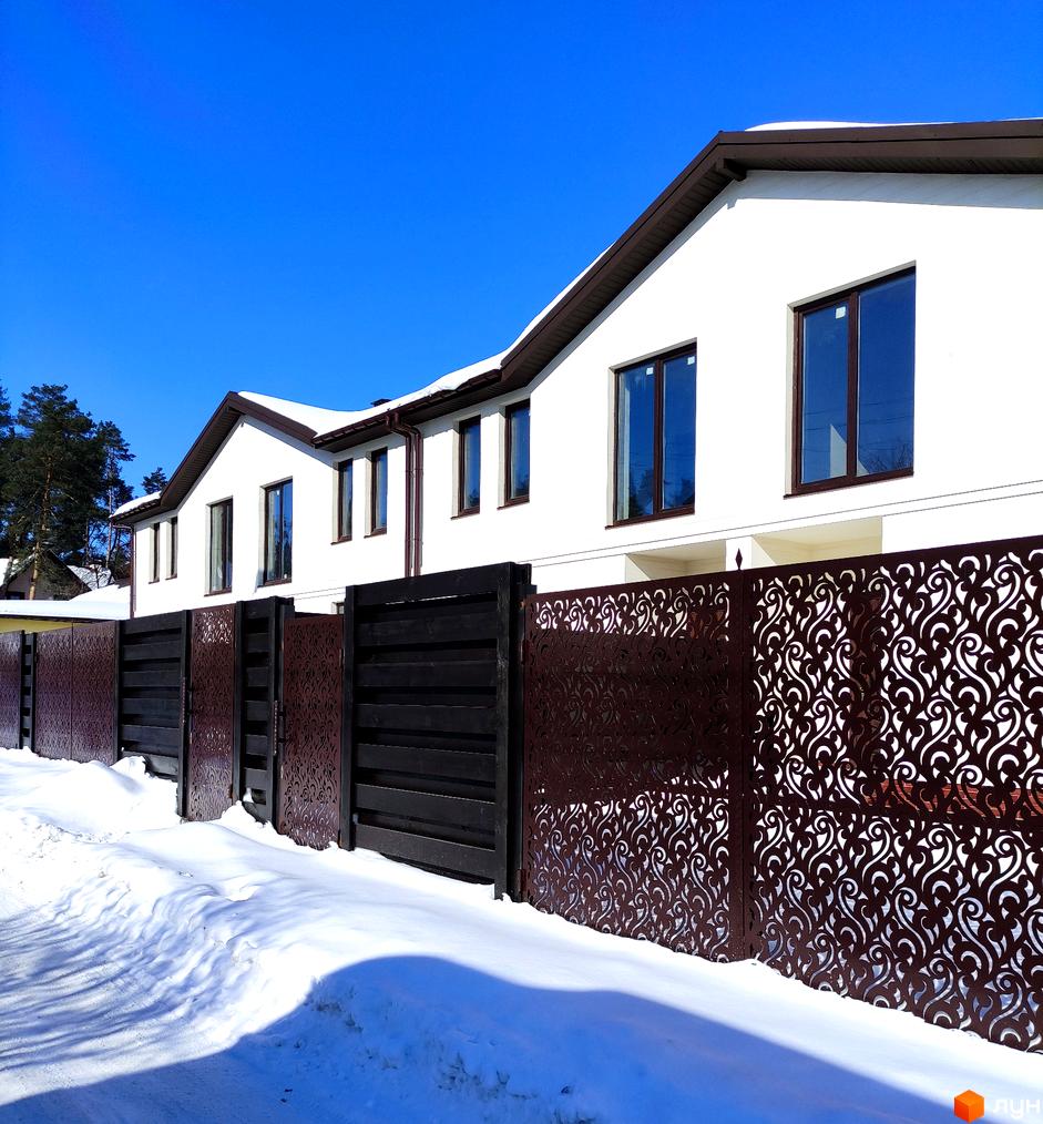 Таунхауси Travertino з білими фасадами та коричневими вікнами на тлі блакитного неба взимку. Огороджені темним парканом з декоративними елементами та засніженою територією.