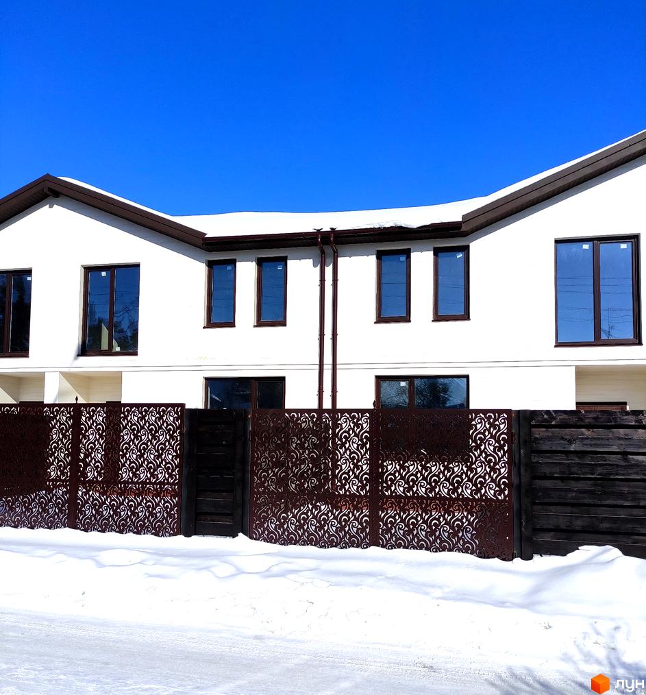 Білий таунхаус Travertino з коричневими вікнами та дахом. Перед будинком декоративний металевий паркан та сніг.