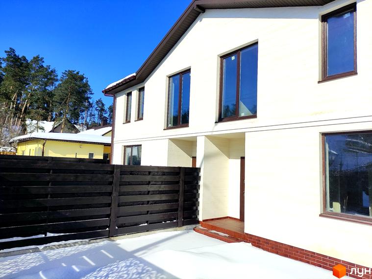 Таунхауси Travertino. Двоповерховий будинок кремового кольору з коричневими віконними рамами та дахом, навколо засніжена територія з темним парканом.