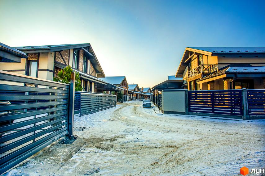 Зимовий пейзаж Котеджного містечка LakeWood з котеджами та засніженою дорогою. Вигляд на будинки з сірими парканами.