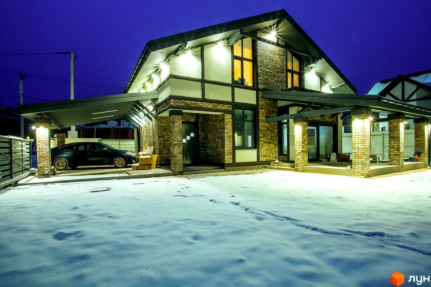 Зображення будинку в Котеджному містечку LakeWood з фасадом з цегли та великими вікнами. Подвір'я вкрито снігом, видно доріжки.