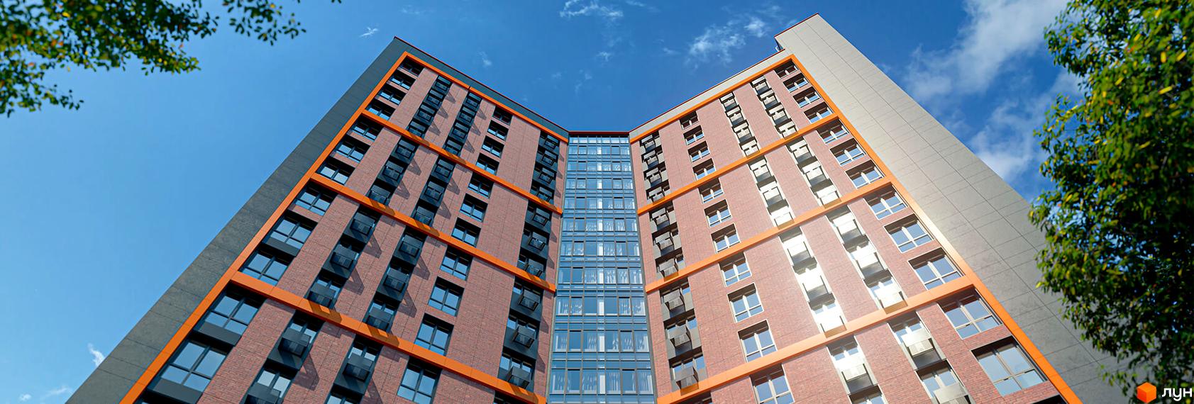 Висотна будівля ЖК Urban One Klochkivska з цегляним фасадом та панорамними вікнами на фоні блакитного неба. Зелені насадження доповнюють архітектуру.