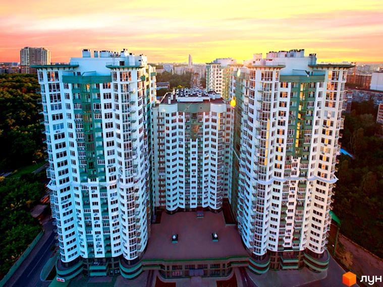 Житловий комплекс Смарагдовий: три висотні будинки білого кольору з зеленими елементами, що оточують внутрішній двір. Навколо комплексу видно зелені насадження та дорогу.