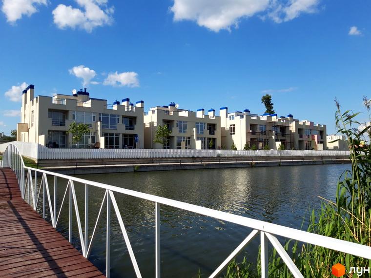 Будинки Lake City біля води з білим парканом та містком. Новобудова з гарною прибудинковою територією.