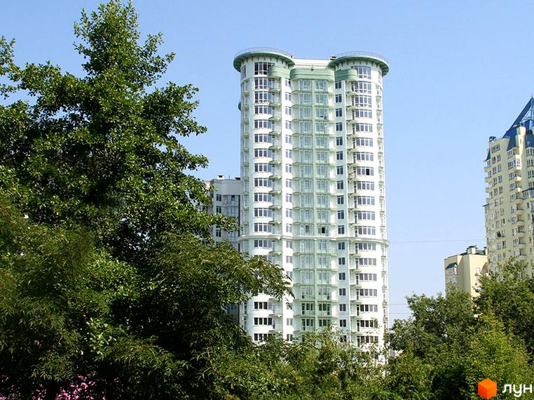 Житловий комплекс Смарагдовий: Високий білий будинок з вигнутими фасадами та зеленими акцентами. Навколо будівель росте багато зелених дерев.