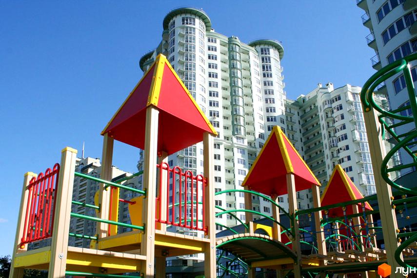 Житловий комплекс Смарагдовий: багатоповерховий будинок зі світлими фасадами. На передньому плані яскравий дитячий майданчик.