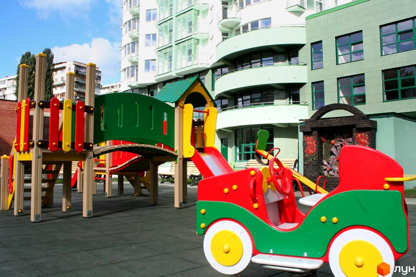 Житловий комплекс Смарагдовий: світлі багатоповерхові будинки з округлими балконами та дитячий майданчик з гірками й гойдалками.