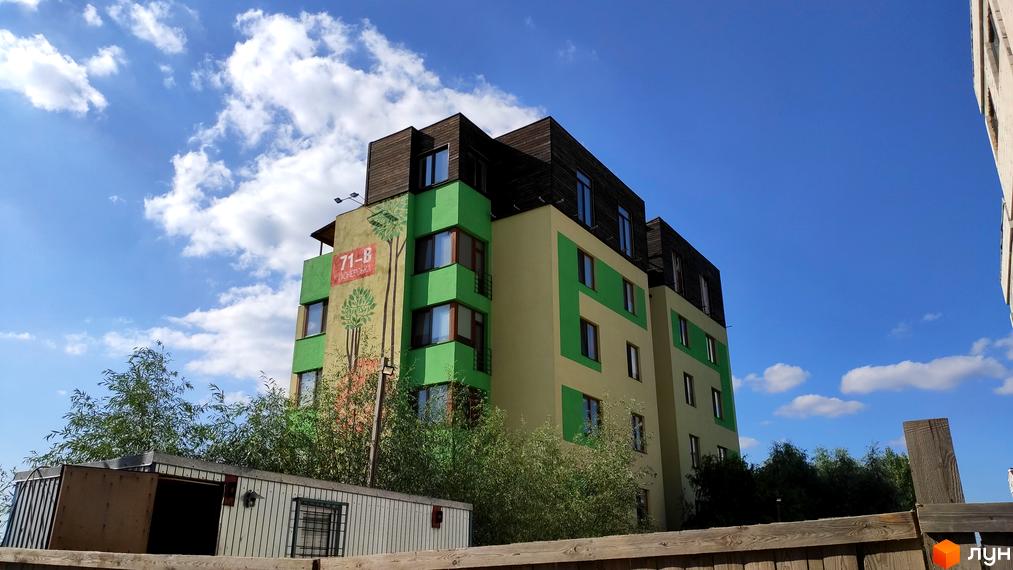 Зовнішній вигляд житлового комплексу Квітневий Дім. Багатоповерховий будинок з зелено-жовтим фасадом та дерев'яним дахом на фоні блакитного неба.