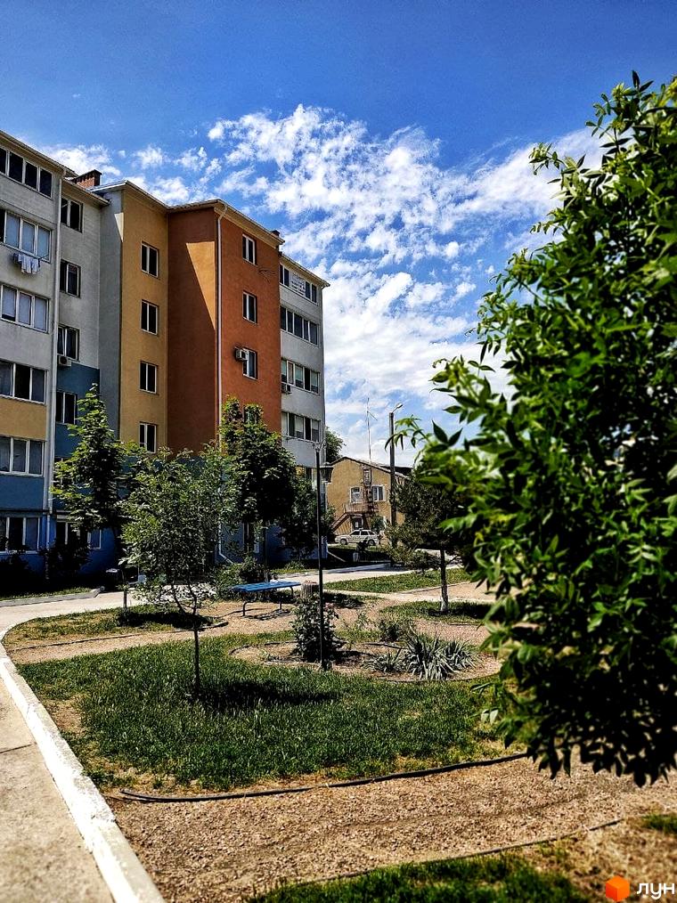 Житловий комплекс Озерки: багатоповерховий будинок з різнокольоровими фасадами та зеленою прибудинковою територією з деревами та лавками.