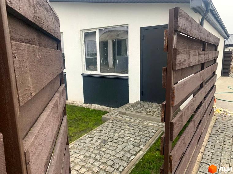 Зовнішній вигляд таунхаусу Белгород з дерев'яним парканом та бруківкою перед входом. Зелена ділянка та вхідні двері з вікном.