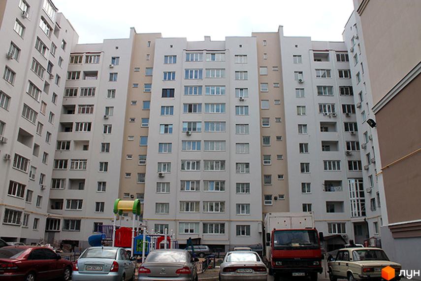 Зовнішній вигляд багатоповерхового житлового комплексу на вул. Бреуса, 61/9. На прибудинковій території видно автомобілі та дитячий майданчик.