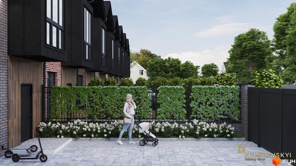 Таунхауси V8 townhouse: фасади з чорними елементами та дерев'яними вставками, зелений паркан з квітами та дитячий візочок на доріжці.