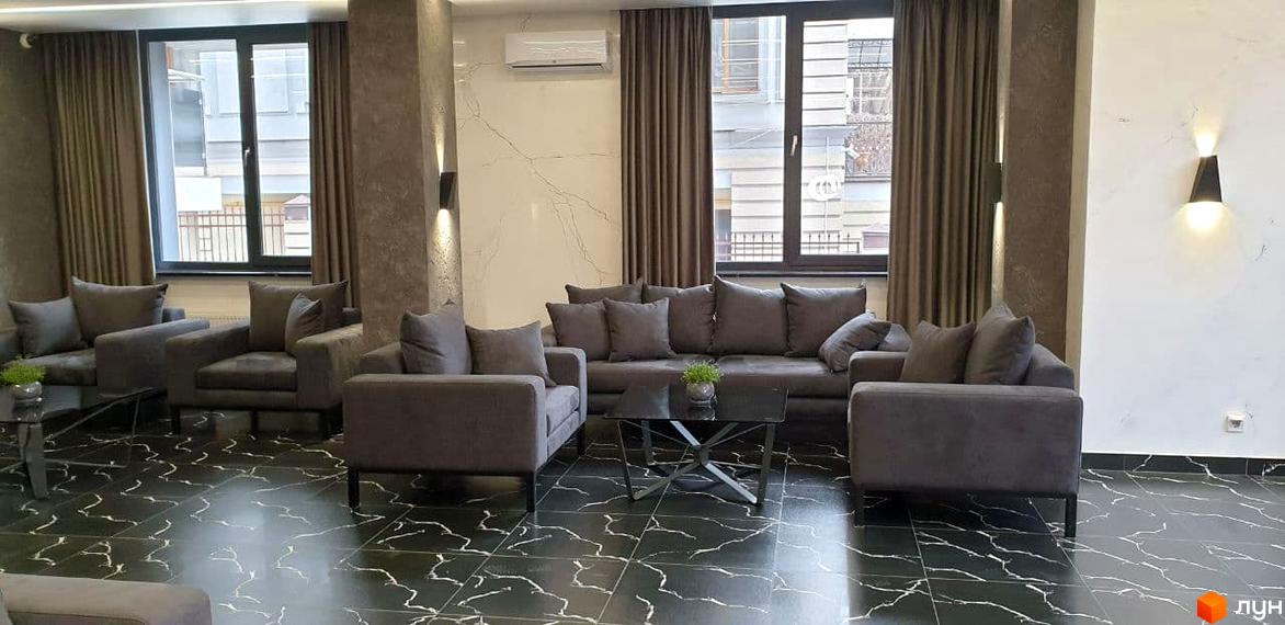 Інтер'єр вітальні в житловому комплексі Зелений замок з сірими диванами та кавовим столиком на чорній мармуровій підлозі. Сучасні меблі та оздоблення створюють затишну атмосферу.