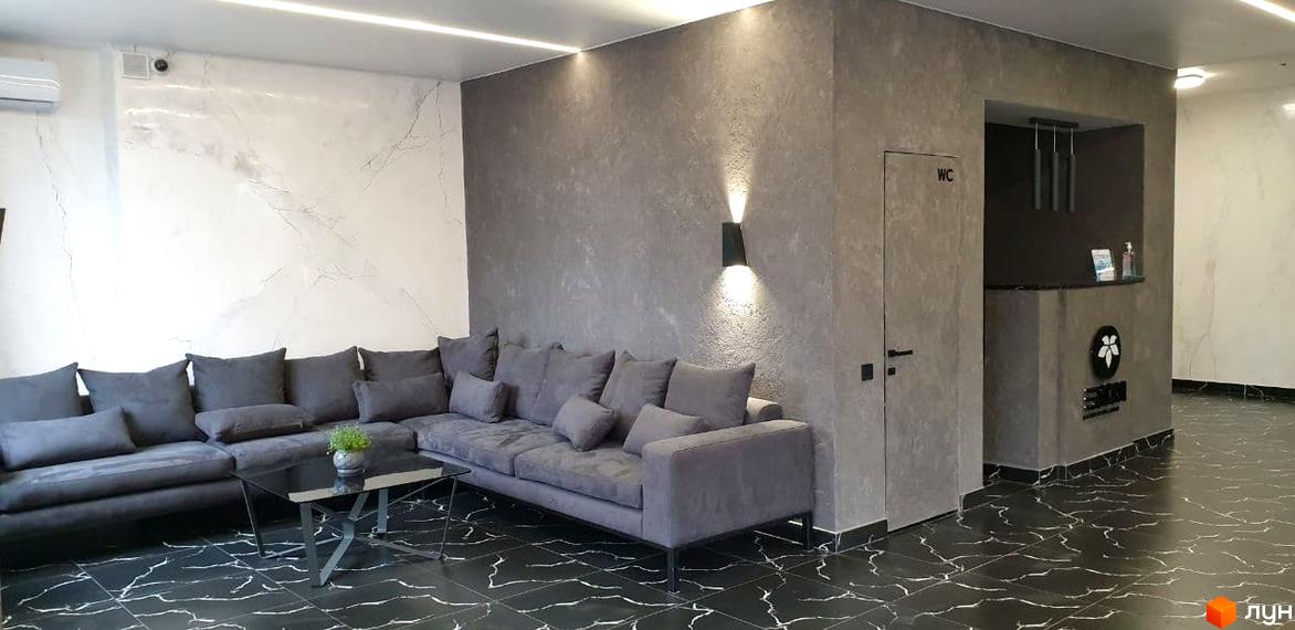 Інтер'єр холу житлового комплексу Зелений замок з сірим диваном та столиком. Сучасний дизайн та оздоблення стін.