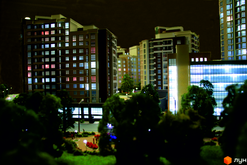 Багатоповерхові будинки Житлового комплексу Французький квартал вночі з освітленими вікнами та зеленими насадженнями.