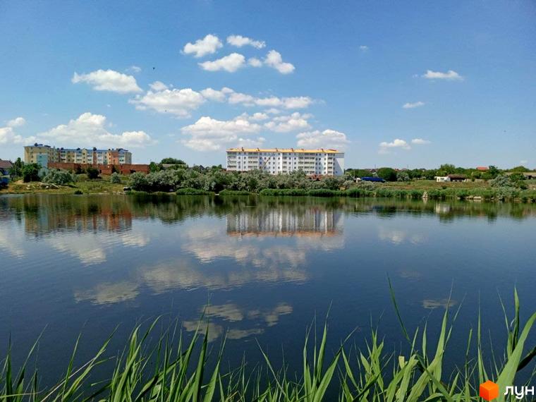 Житловий комплекс Озерки - багатоповерхові будинки біля озера з відображенням хмар у воді. Зелена територія та водний простір.