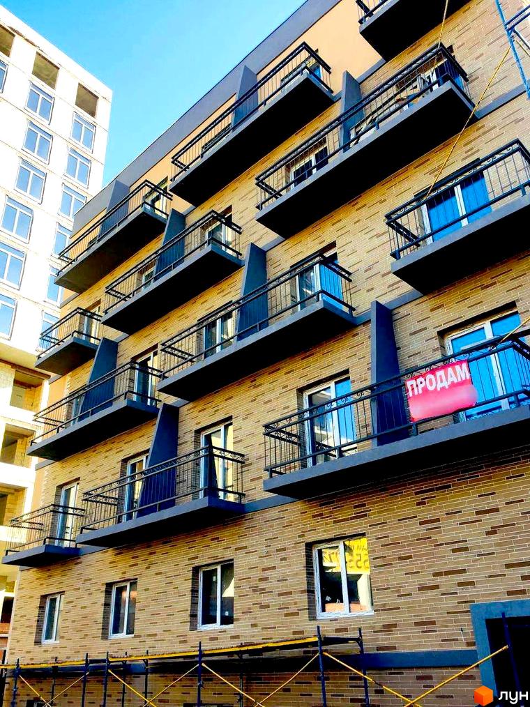 Зовнішній вигляд житлового комплексу Свобода-2 з балконами та вікнами на тлі блакитного неба. Будівельний проєкт з цегляним фасадом.