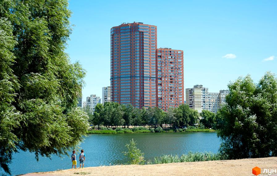 Житловий комплекс Ревуцького, 9 з сучасним фасадом на фоні водойми та зелених насаджень. Прибудинкова територія з деревами та відпочинковими зонами.