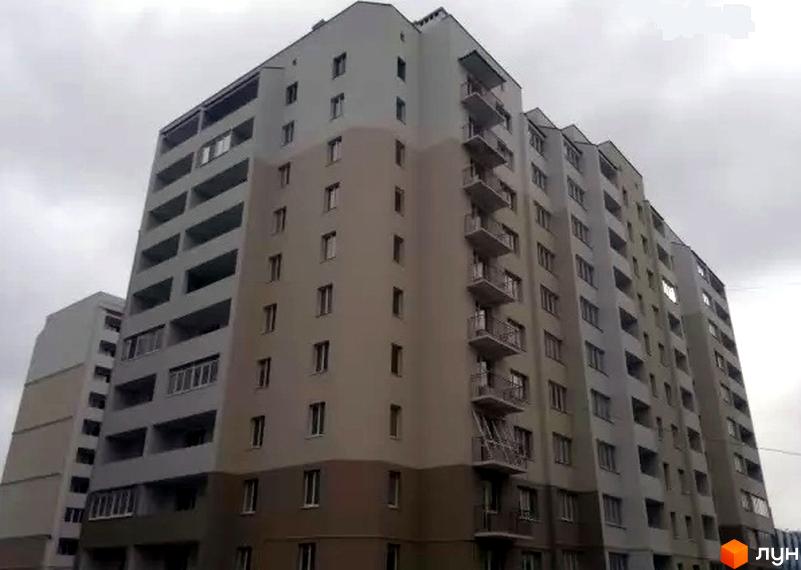 Багатоповерховий житловий комплекс на вул. Бреуса, 61/9, з сірими та бежевими фасадами, балконами та багатьма вікнами. Будинок має сучасну архітектуру та виглядає акуратно.