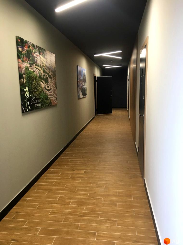 Коридор у новобудові ЖК CENTRAL HOUSE з дерев'яною підлогою та картинами на стінах. Оздоблення стін та стелі виконано в нейтральних тонах, що створює затишну атмосферу.