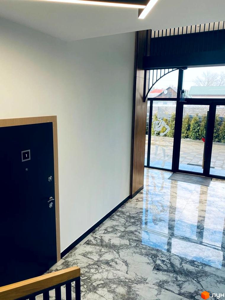 Сучасний вхід у житловий комплекс CENTRAL HOUSE з мармуровою підлогою та великими скляними дверима, що ведуть на подвір'я з деревами.