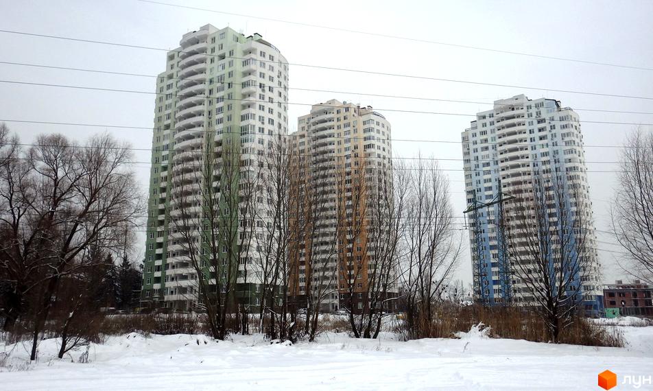 Зовнішній вигляд житлового комплексу Озерний (Обухівська, 135а) взимку. Три висотні будинки з балконами на тлі хмарного неба та дерев у снігу.