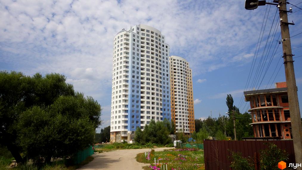 Житловий комплекс Озерний (Обухівська, 135а) - висотні будинки з білою та блакитною облицовкою, поруч зелені дерева та квітуча територія.