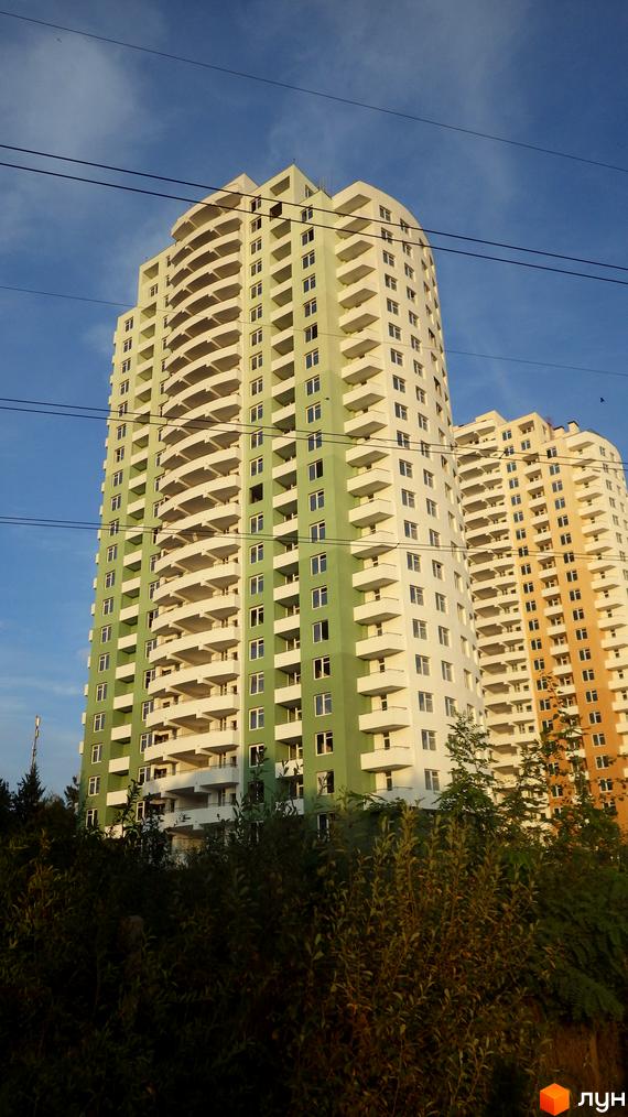 Житловий комплекс Озерний. Зелена та жовта новобудови з численними балконами на тлі блакитного неба. Навколо видно зелені насадження.