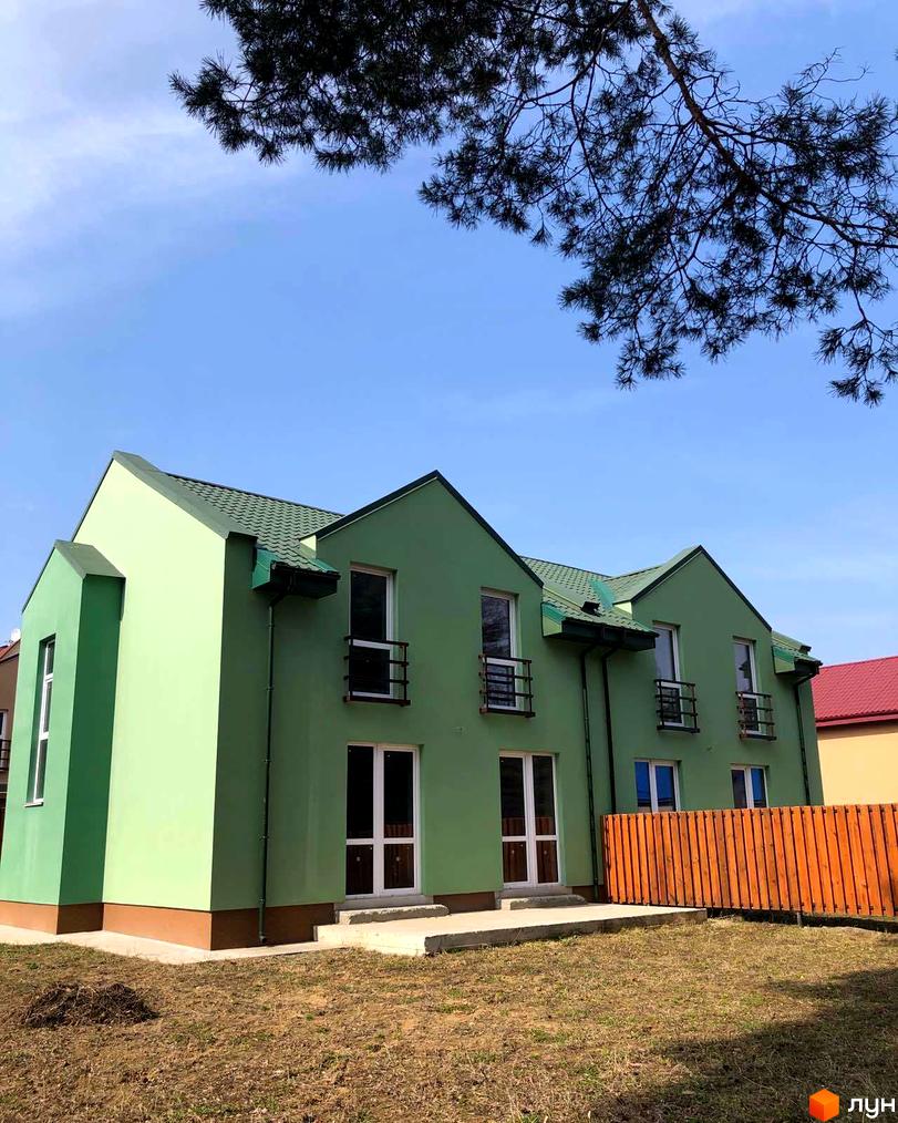 Котеджне містечко Sunny Village: зелений будинок з металочерепичним дахом, вікнами з декоративними огорожами та прибудинковою територією з газоном і дерев'яним парканом.