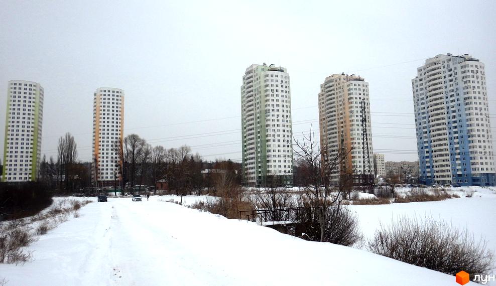 Житловий комплекс Озерний (Обухівська, 135а) - висотні будинки з білими фасадами та кольоровими вставками на тлі хмарного неба. Навколо засніжена територія з деревами та доріжкою.