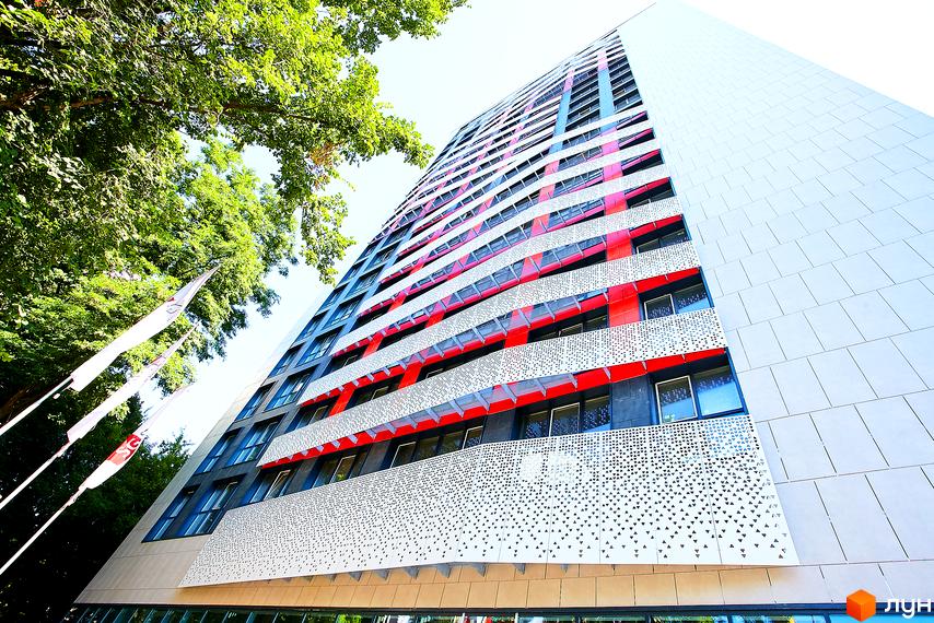 Фасад житлового комплексу Квартет з червоними та білими елементами, вікнами та перфорованими панелями. Поруч зелені дерева та прапори.