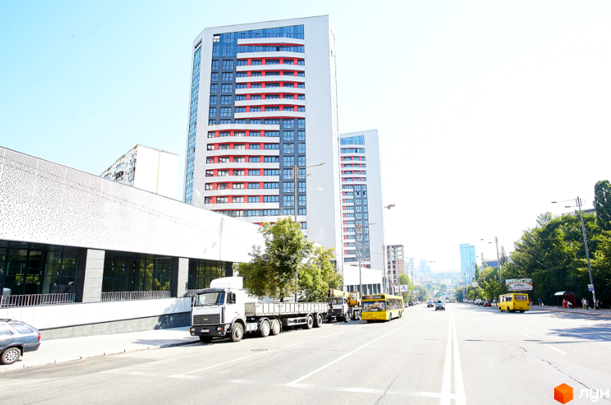 Житловий комплекс Квартет. Сучасна архітектура з червоними та сірими фасадами, великими вікнами. Поруч дорога з автомобілями та автобусами.