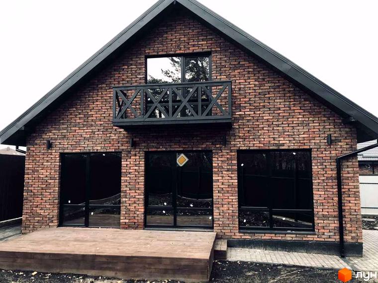Котеджне містечко КМ Одноповерховий Київ - Нові Петрівці. Фасад будинку з червоної цегли, великі чорні вікна, дерев'яна тераса.