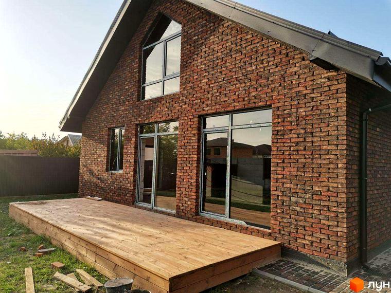 Котеджне містечко КМ Одноповерховий Київ - Нові Петрівці. Зовнішній вигляд будинку з цегляним фасадом та дерев'яною терасою.