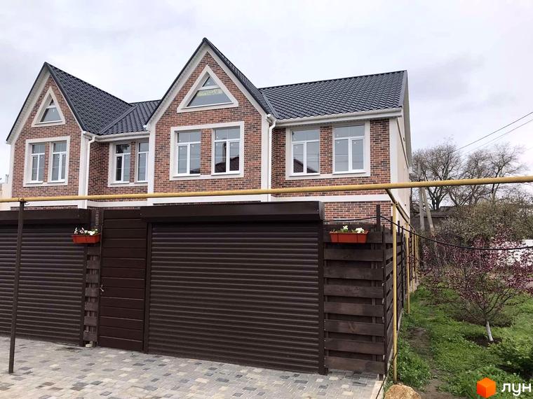 Таунхауси CLEVER: двоповерхові цегляні будинки з темним дахом та білими вікнами, огороджені коричневим парканом з ролетними воротами. Прибудинкова територія з деревами та зеленню.