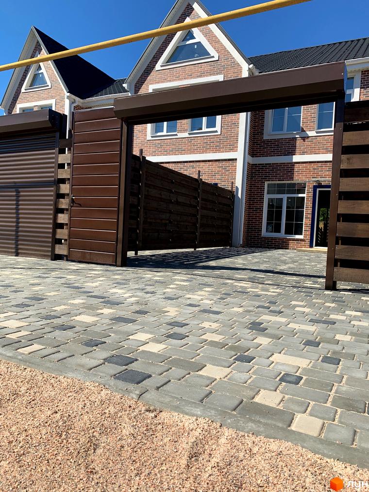 Таунхауси CLEVER з цегляним фасадом та брукованою прибудинковою територією. Відкриті ворота та паркан з дерев'яних ламелей.