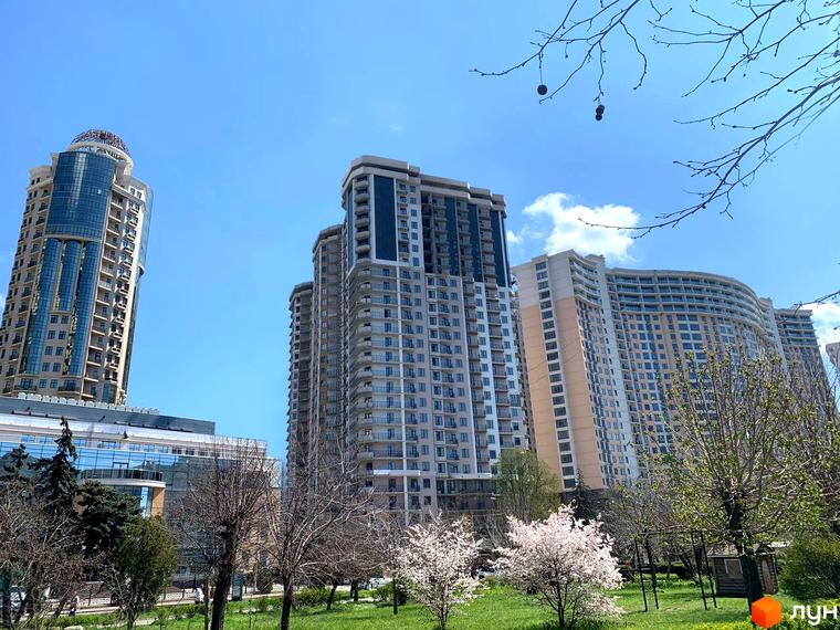 Високі будинки житлового комплексу Родос з великими вікнами. На передньому плані зелена трава та дерева.