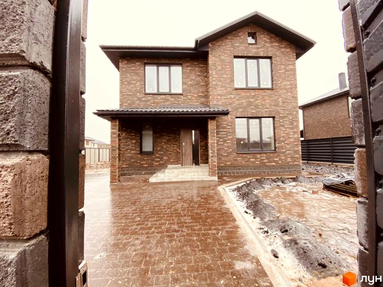 Котеджне містечко КМ Весняний: цегляний двоповерховий будинок з великими вікнами та вимощеним подвір'ям. Навколо будинку облаштована прибудинкова територія.