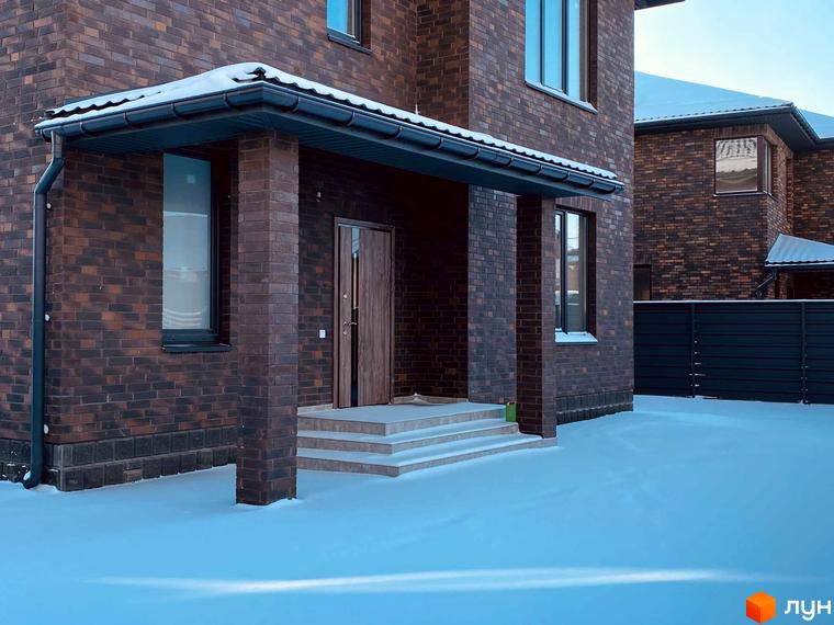 Котеджне містечко КМ Весняний. Зовнішній вигляд будинку з коричневої цегли під час снігопаду, вхідна група з дверима та сходами.