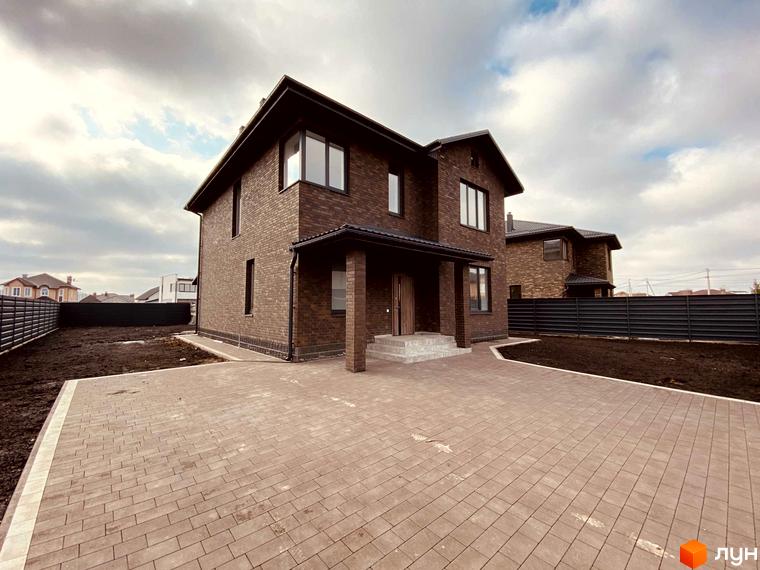 Котеджне містечко КМ Весняний: двоповерховий цегляний будинок з великими вікнами та вимощеною прибудинковою територією. Навколо огороджена ділянка з грунтом.