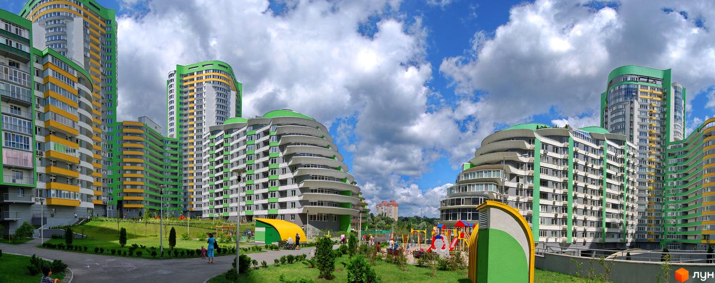 Житловий комплекс Паркове місто з високими будинками зелено-жовтого кольору та доглянутою прибудинковою територією з дитячим майданчиком.