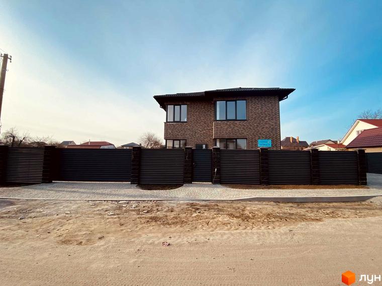 Котеджне містечко КМ Весняний: двоповерховий цегляний будинок з великими вікнами, огороджений темним парканом з цегляними стовпами.