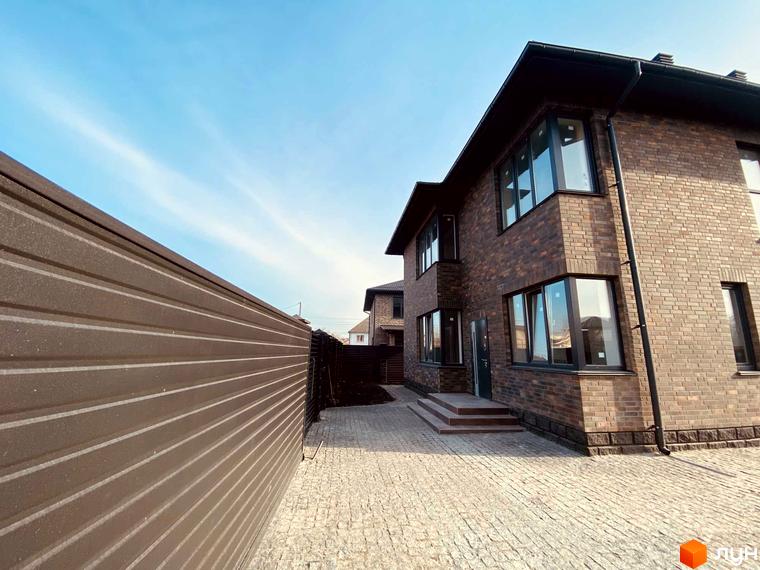 Котеджне містечко КМ Весняний: двоповерховий будинок з цегляним фасадом та великими вікнами, вимощена бруківкою прибудинкова територія.