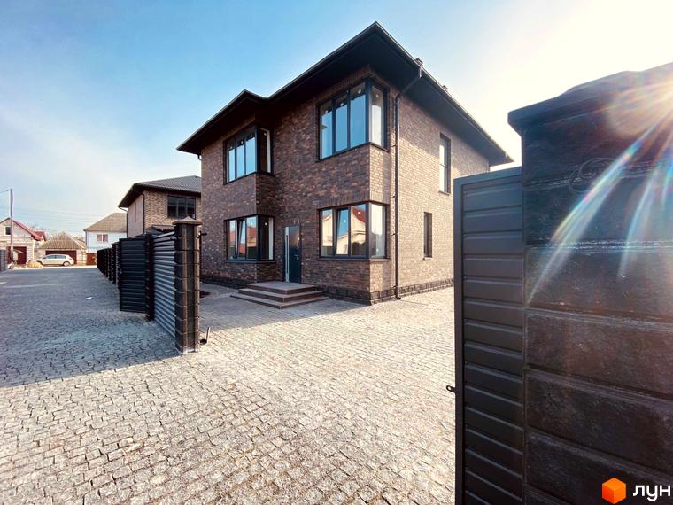 Котеджне містечко Весняний: двоповерховий будинок з цегляним фасадом та бруківкою на території. Навколо огороджена територія з парканом.