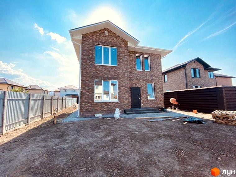 Котеджне містечко КМ Весняний: двоповерховий будинок з цегляним фасадом та великими вікнами, огороджена територія з будматеріалами.