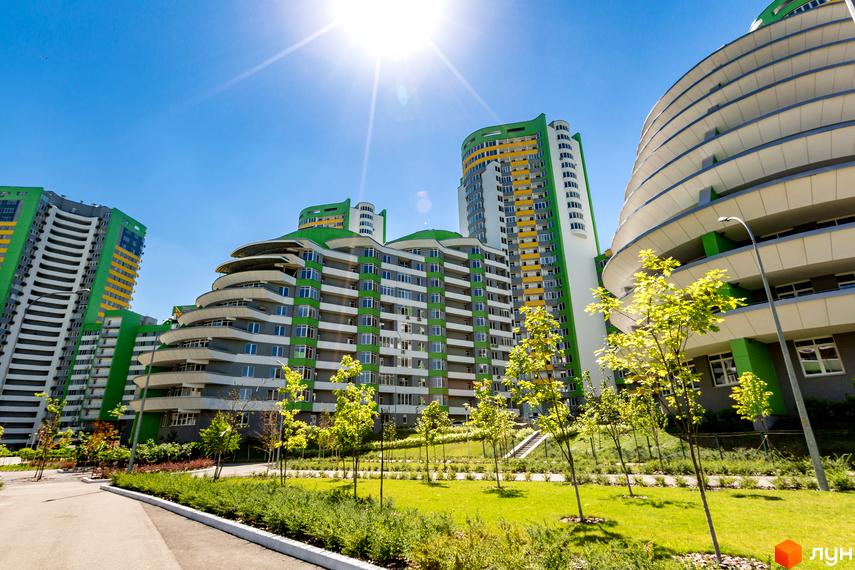 Житловий комплекс Паркове місто: багатоповерхові будинки з фасадами зеленого, сірого та жовтого кольорів. Прибудинкова територія має зелені газони та молоді дерева.