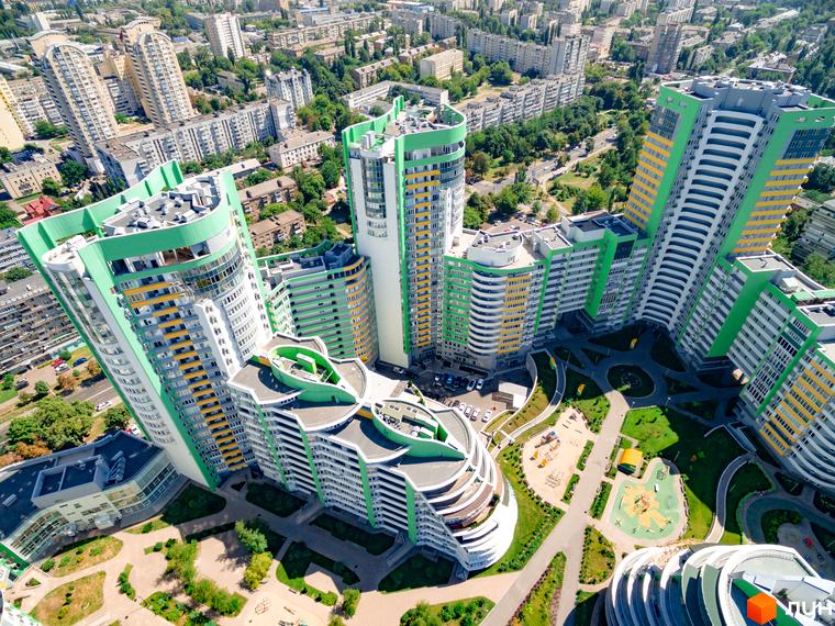 Житловий комплекс Паркове місто з висотними будинками світлих відтінків з зеленими акцентами. На території комплексу облаштовані зелені зони та дитячі майданчики.