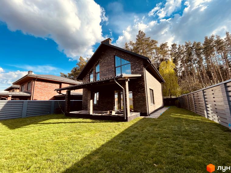 Котеджне містечко КМ Лісова Білогородка. Фасад будинку з темної цегли, великі вікна, тераса та зелений газон.
