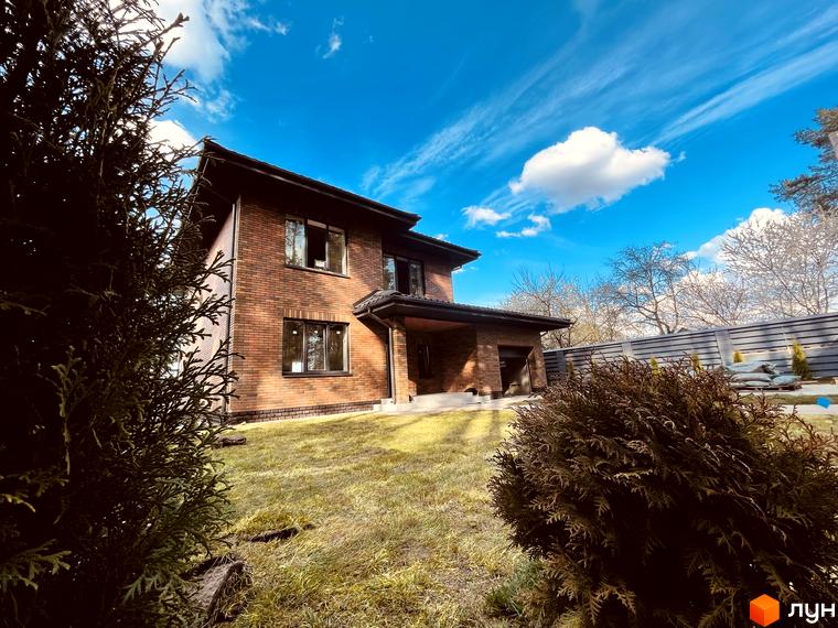 Котеджне містечко КМ Лісова Білогородка: цегляний двоповерховий будинок з вікнами та навісом, зелена галявина та огорожа на прибудинковій території.