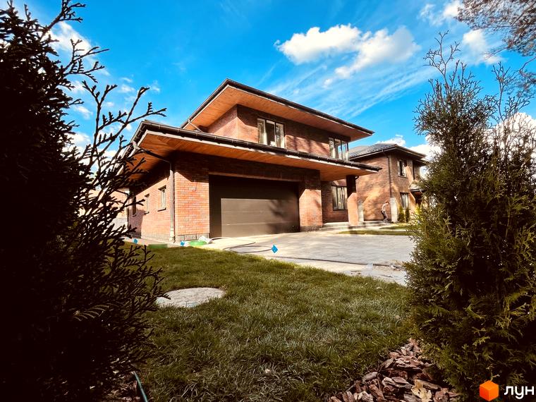 Котеджне містечко КМ Лісова Білогородка. Фасад будинку з червоної цегли з великим гаражем та доглянутою зеленою ділянкою.